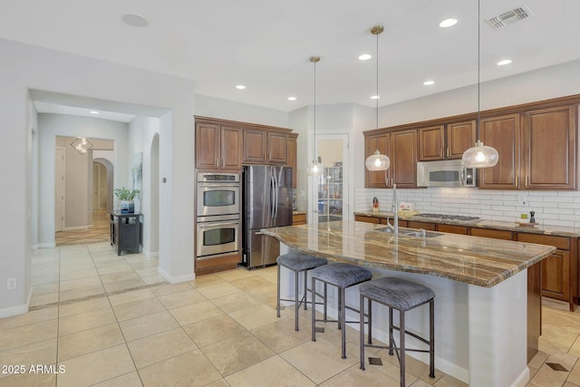 kitchen featuring a center island with sink, stone countertops, hanging light fixtures, and appliances with stainless steel finishes