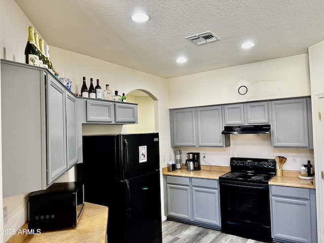 10489 S 182nd Dr, Goodyear, AZ 85338 - kitchen featuring light wood-style floors, under cabinet range hood, gray cabinetry, and black appliances