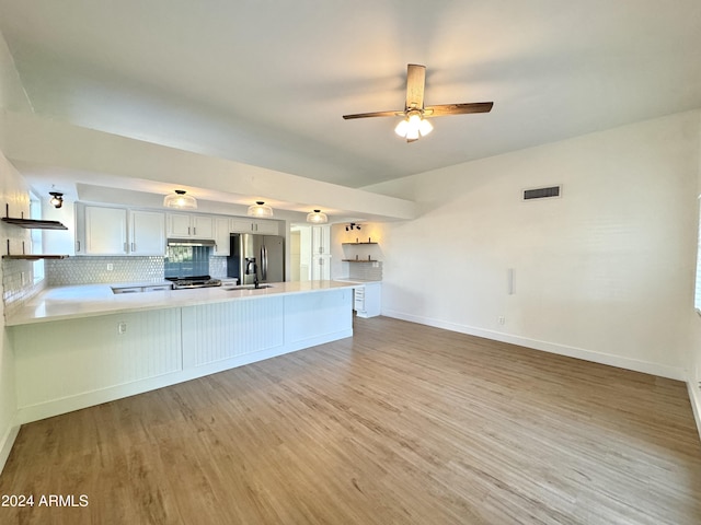 kitchen with sink, stainless steel fridge, kitchen peninsula, white cabinets, and decorative backsplash