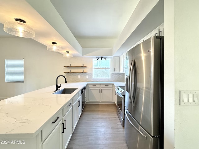 kitchen with stainless steel appliances, light stone counters, white cabinets, sink, and kitchen peninsula