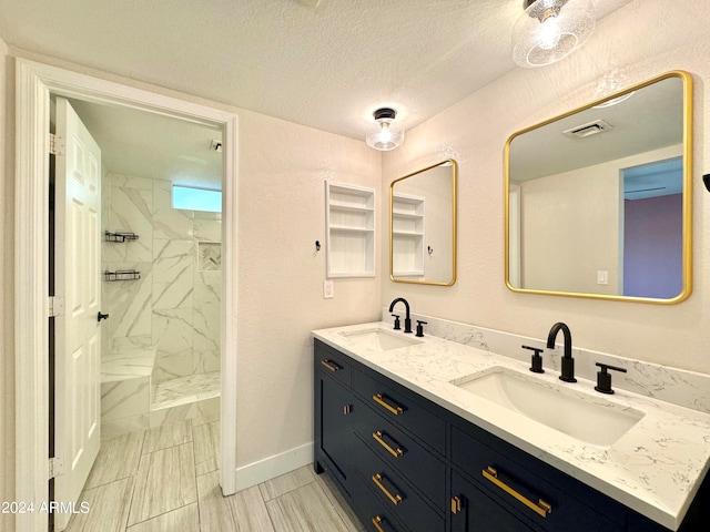 bathroom with dual vanity, a textured ceiling, a tile shower, and tile patterned floors