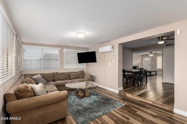 living room with a wall unit AC, ceiling fan, and dark wood-type flooring