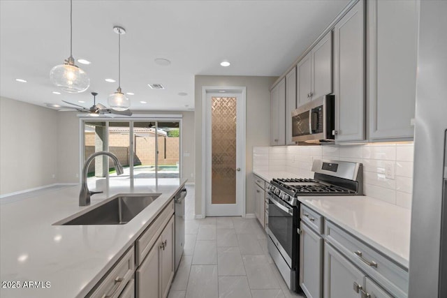 kitchen with gray cabinetry, appliances with stainless steel finishes, a sink, and tasteful backsplash