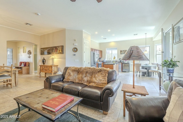 living room with visible vents, ornamental molding, recessed lighting, arched walkways, and light tile patterned floors