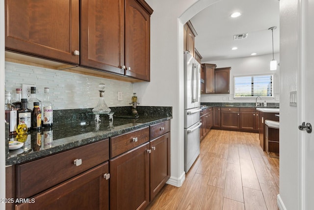 kitchen featuring pendant lighting, decorative backsplash, stainless steel refrigerator, light wood-type flooring, and dark stone counters