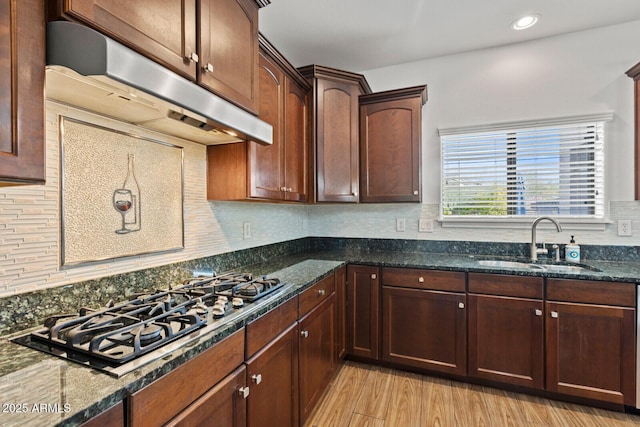 kitchen featuring stainless steel gas cooktop, light wood-type flooring, dark stone counters, and sink