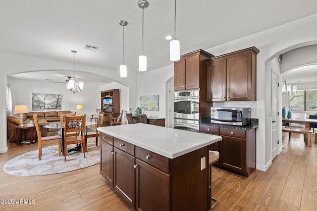 kitchen with light hardwood / wood-style floors, appliances with stainless steel finishes, decorative light fixtures, dark brown cabinets, and a kitchen island