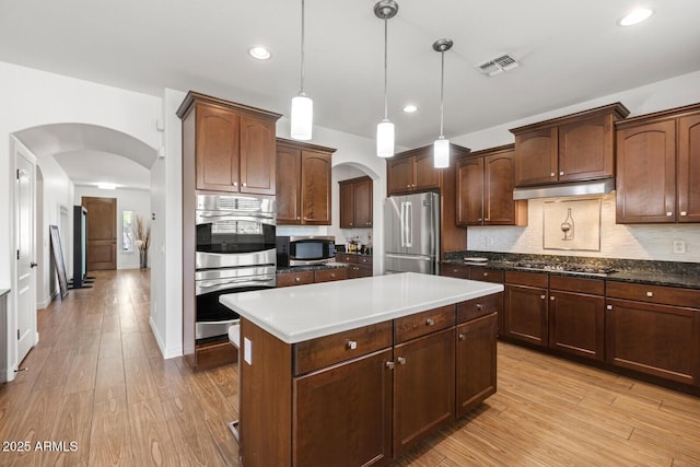 kitchen featuring decorative light fixtures, backsplash, stainless steel appliances, and light hardwood / wood-style flooring