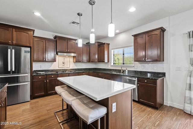 kitchen with appliances with stainless steel finishes, a center island, decorative light fixtures, sink, and light hardwood / wood-style flooring