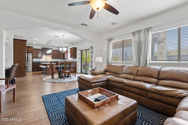 living room with ceiling fan with notable chandelier and light hardwood / wood-style flooring