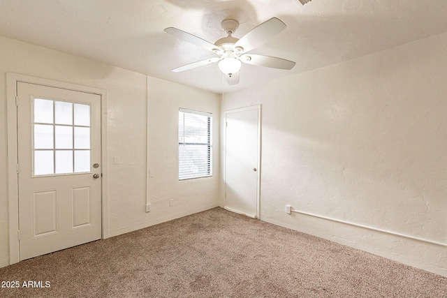 unfurnished room with a textured wall, carpet flooring, and a ceiling fan