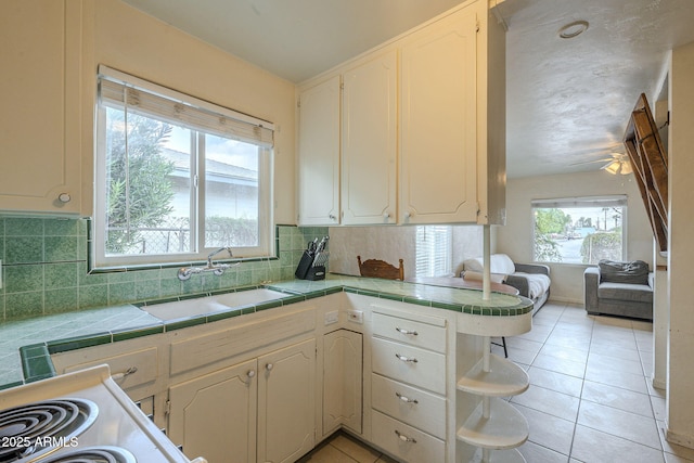 kitchen featuring light tile patterned floors, tasteful backsplash, tile counters, a sink, and a peninsula