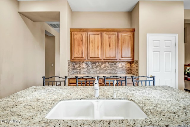 kitchen with visible vents, light stone counters, backsplash, and a sink