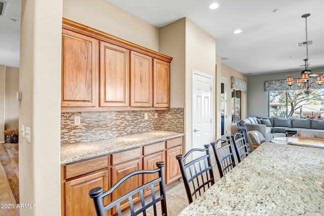 kitchen featuring light stone counters, visible vents, open floor plan, hanging light fixtures, and tasteful backsplash