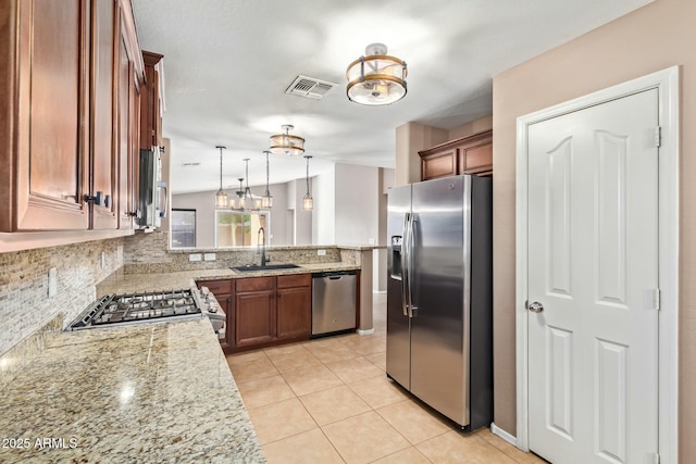 kitchen featuring stainless steel appliances, a sink, light stone countertops, brown cabinetry, and pendant lighting