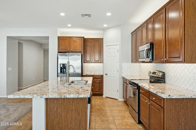 kitchen with light tile patterned floors, stainless steel appliances, a sink, visible vents, and an island with sink