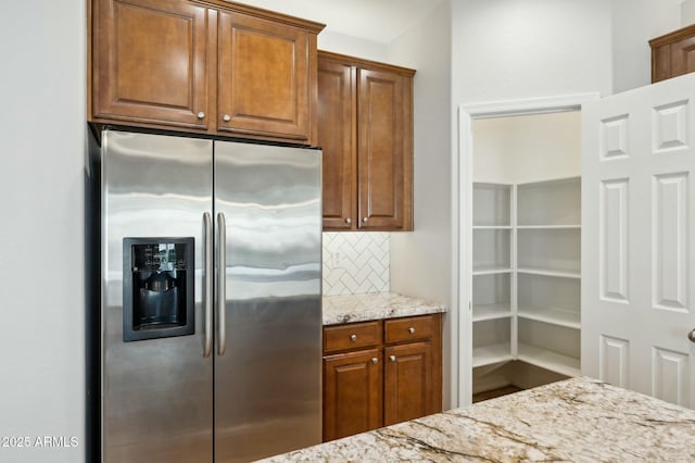 kitchen featuring light stone counters, brown cabinets, backsplash, and stainless steel fridge with ice dispenser