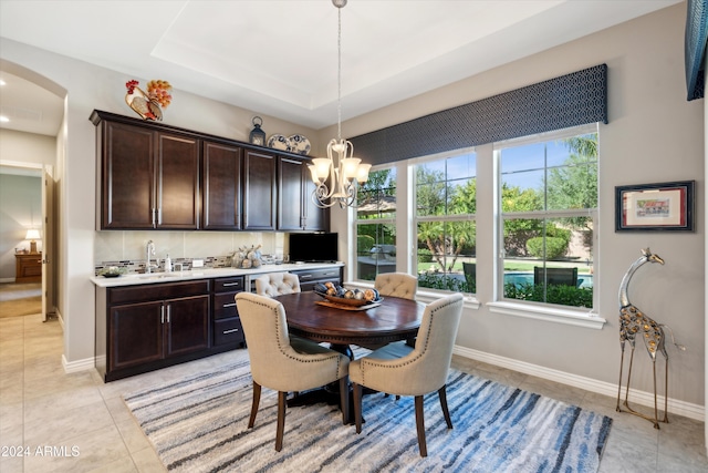 tiled dining space with sink, a raised ceiling, and a chandelier