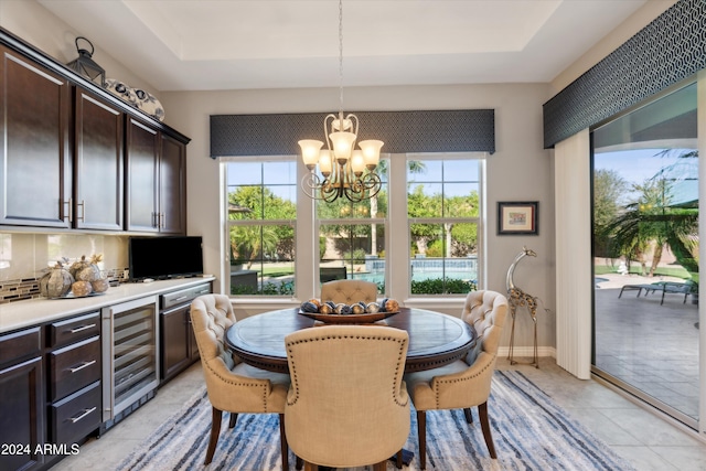 tiled dining room with a tray ceiling, a chandelier, beverage cooler, and a healthy amount of sunlight