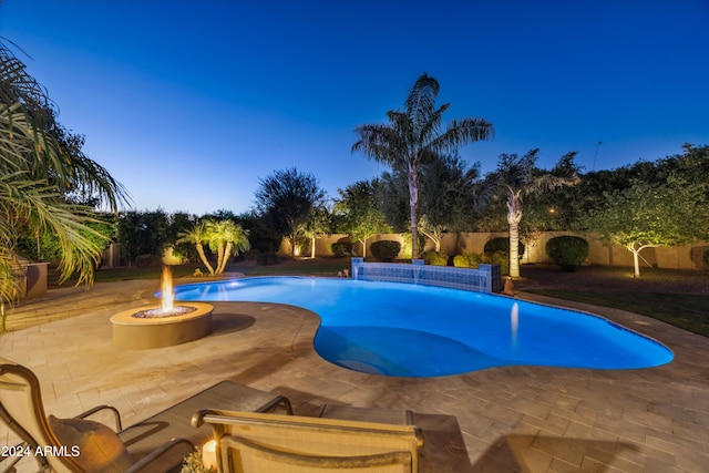 pool at dusk with a patio, pool water feature, and a fire pit