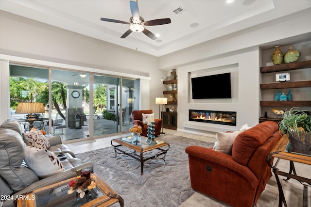 tiled living room with ceiling fan and a tray ceiling