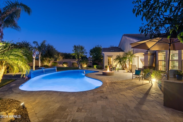 pool at twilight with pool water feature, an outdoor fire pit, and a patio area