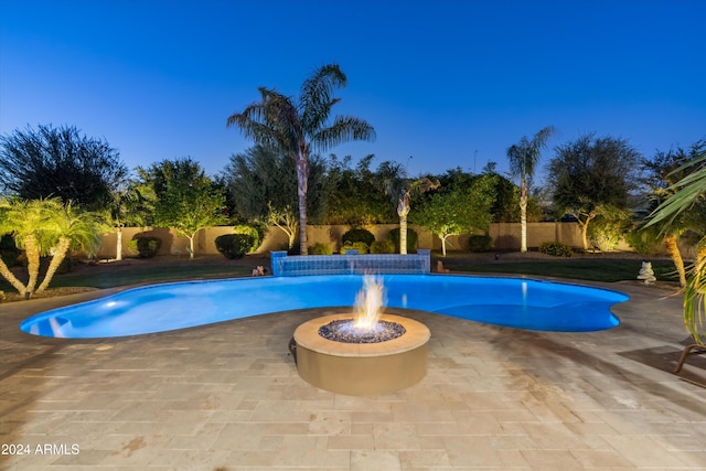 pool at dusk with a patio, pool water feature, and a fire pit