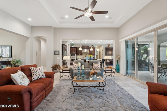 tiled living room with ceiling fan and a tray ceiling