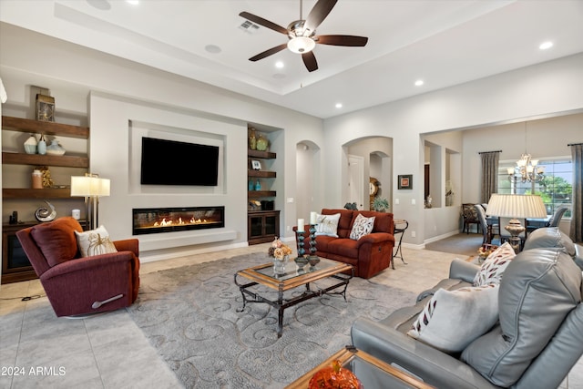 living room with light tile patterned flooring, a raised ceiling, ceiling fan with notable chandelier, and built in features