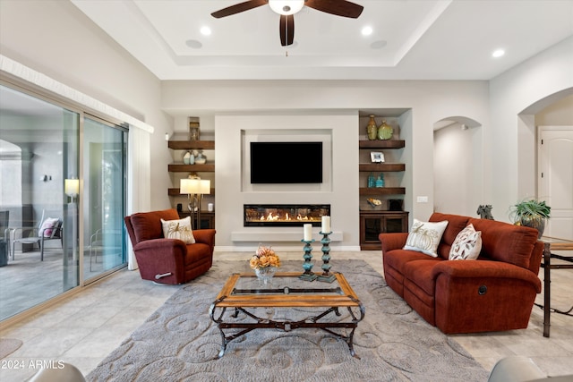 living room with ceiling fan, a tray ceiling, and built in features