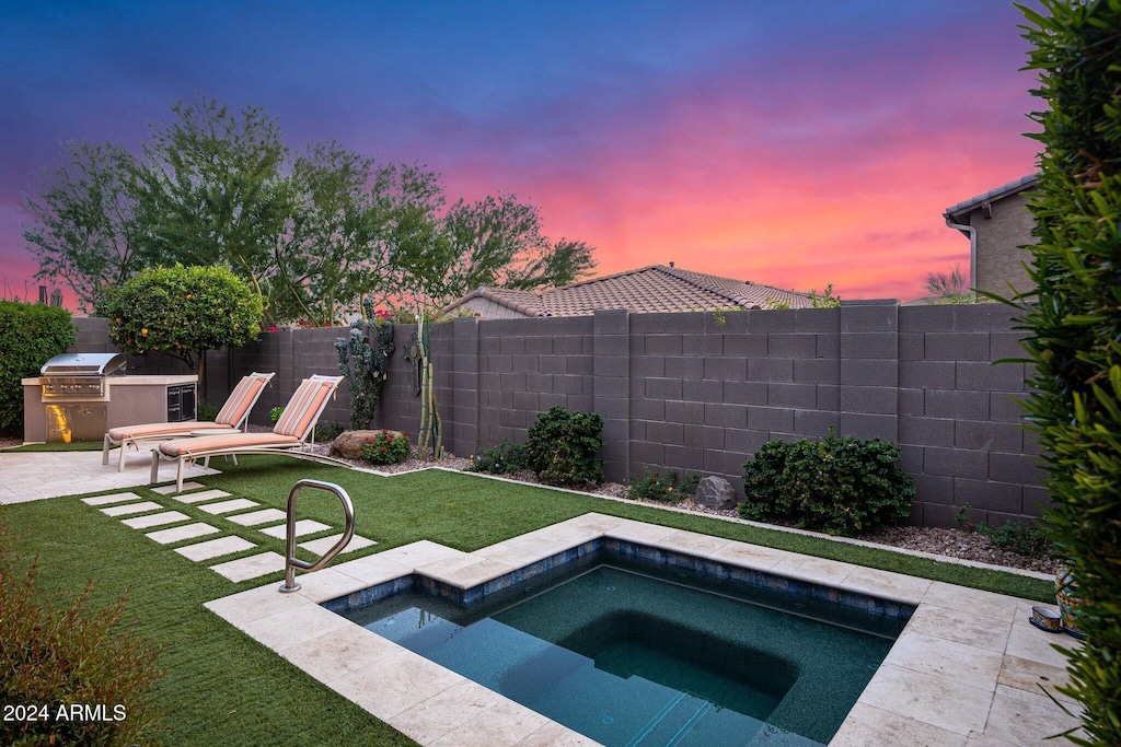 pool at dusk with area for grilling, a lawn, a patio area, and exterior kitchen