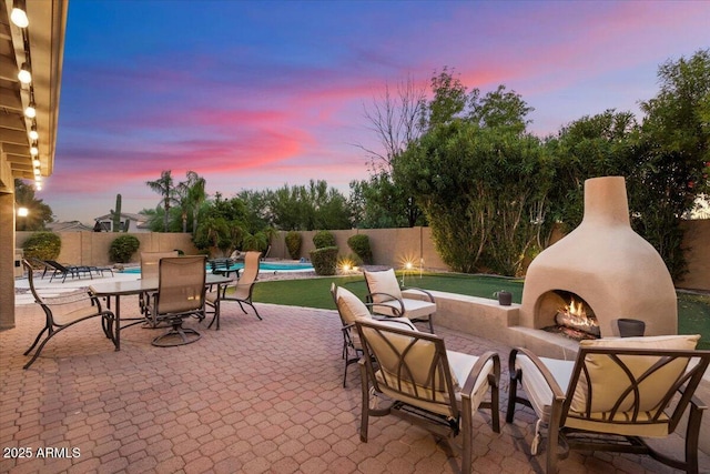 7471 E Desert Vista Rd, Scottsdale, AZ 85255 - patio terrace at dusk featuring a warm lit fireplace, a fenced in pool, and a fenced backyard