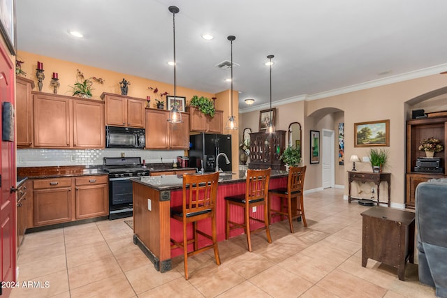 kitchen featuring a kitchen breakfast bar, hanging light fixtures, a kitchen island with sink, black appliances, and crown molding