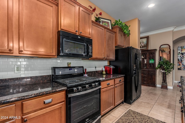 kitchen with black appliances, ornamental molding, light tile patterned floors, and dark stone counters