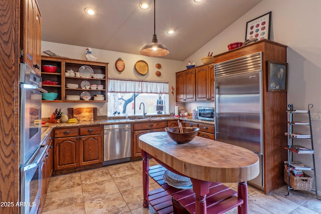 kitchen featuring lofted ceiling, sink, light stone counters, pendant lighting, and stainless steel appliances