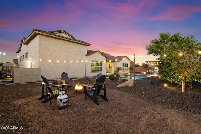 18577 W Coolidge St, Goodyear, AZ 85395 - back of house at dusk featuring an outdoor fire pit, stucco siding, and a patio