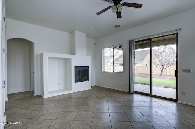 unfurnished living room with a glass covered fireplace, tile patterned floors, arched walkways, and visible vents