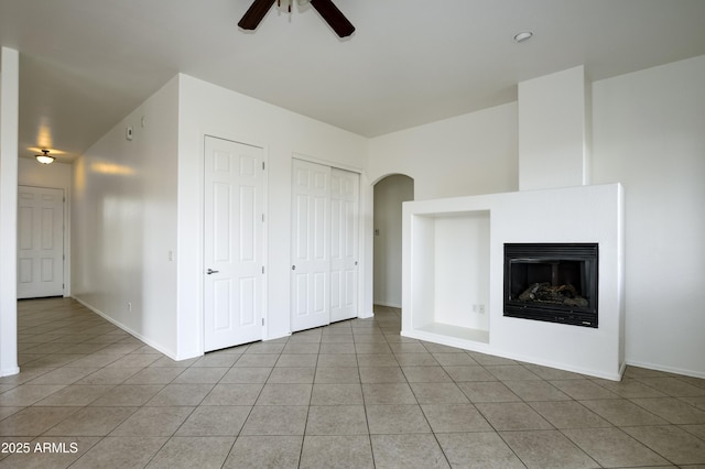 unfurnished living room featuring a glass covered fireplace, light tile patterned floors, a ceiling fan, and baseboards