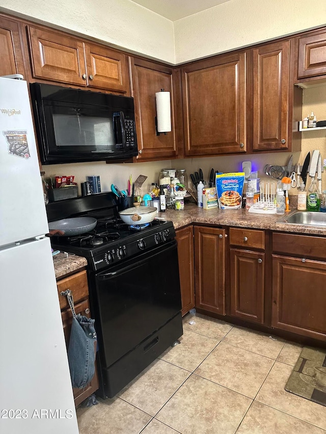 kitchen featuring light tile flooring, black appliances, and dark stone countertops