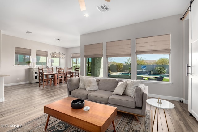 living room featuring wood finished floors, visible vents, baseboards, and a barn door