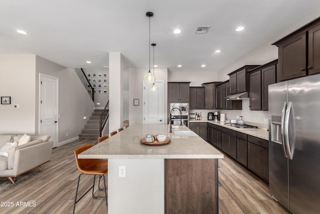 kitchen with appliances with stainless steel finishes, a sink, light wood-style floors, and a kitchen breakfast bar