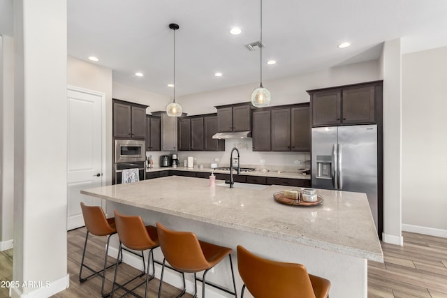 kitchen featuring dark brown cabinetry, visible vents, light wood-style flooring, stainless steel appliances, and a kitchen bar