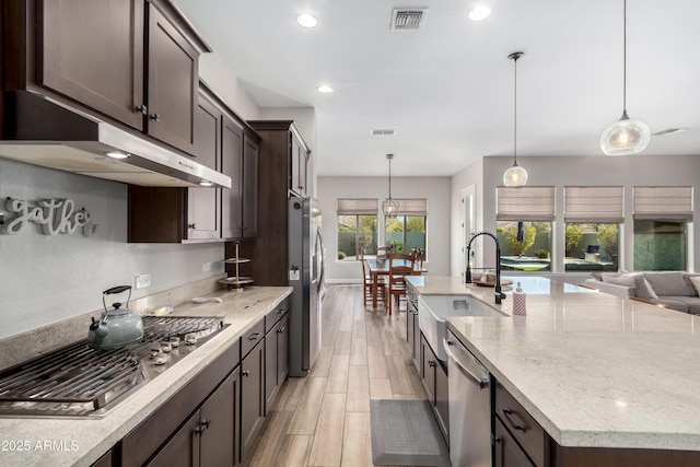 kitchen featuring stainless steel appliances, visible vents, dark brown cabinetry, a sink, and light stone countertops