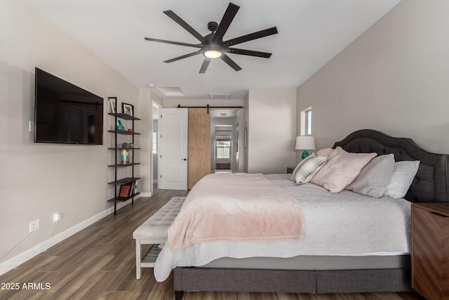 bedroom featuring a barn door, wood finished floors, a ceiling fan, visible vents, and baseboards