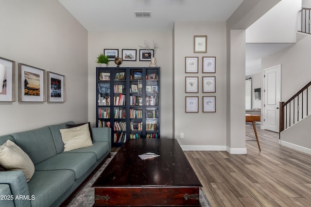 living area with stairway, wood finished floors, visible vents, and baseboards