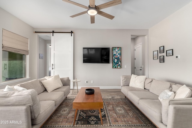 living area featuring a barn door, wood finished floors, a ceiling fan, and baseboards