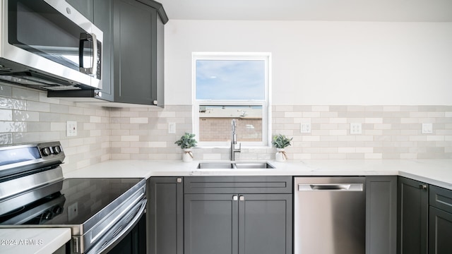 kitchen with gray cabinetry, backsplash, sink, appliances with stainless steel finishes, and light stone counters