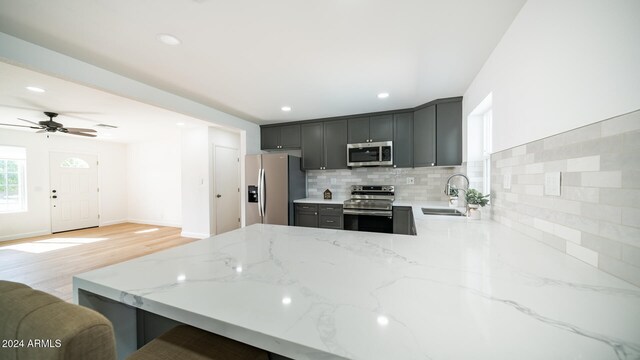 kitchen featuring kitchen peninsula, stainless steel appliances, light stone counters, and sink