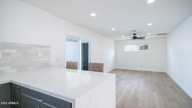 kitchen with backsplash, ceiling fan, light wood-type flooring, light stone countertops, and kitchen peninsula