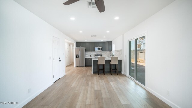 kitchen with a kitchen breakfast bar, ceiling fan, light wood-type flooring, and appliances with stainless steel finishes